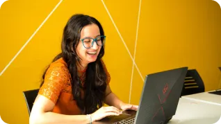 Jeune femme souriante sur fond jaune avec son pc pour le bootcamp marketing digital chez gomycode