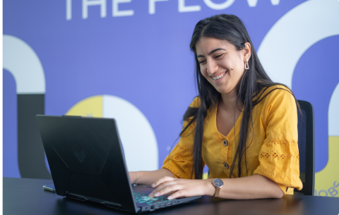 Femme souriante devant son ordinateur sous fond violet pour le cours sur la generative IA